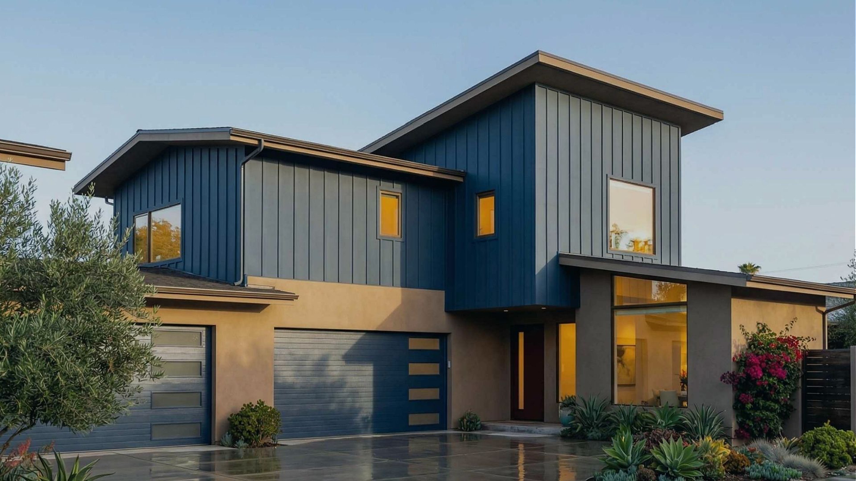 Modern two-story home with blue vertical siding and warm-lit windows, built by ATP